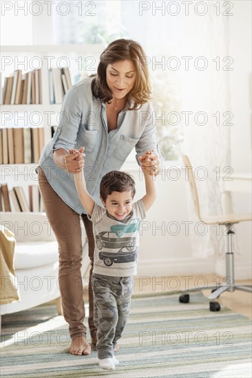 Mother holding son (2-3) making first steps.