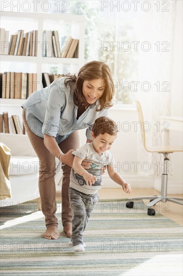 Mother holding son (2-3) making first steps.