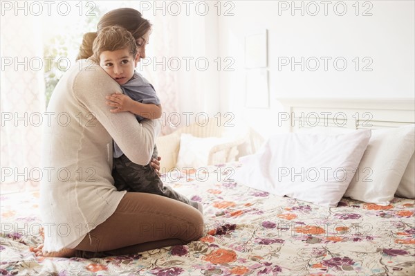 Mother embracing son (2-3) on bed.