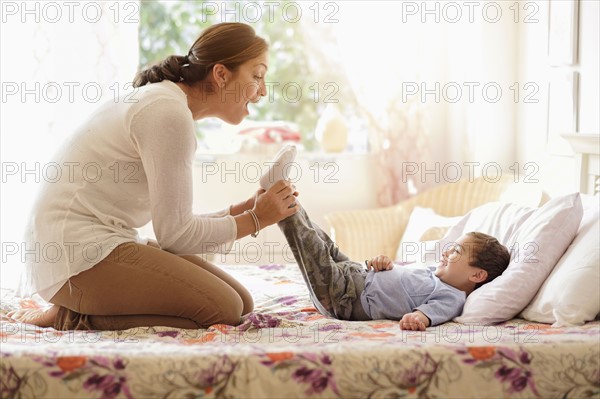 Mother playing with son (2-3) on bed.