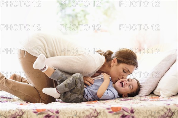 Mother playing with son (2-3) on bed.