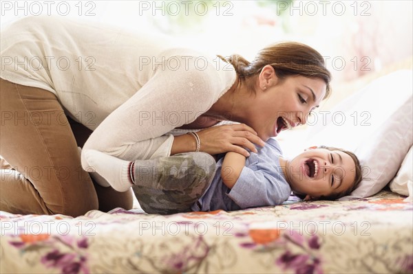 Mother playing with son (2-3) on bed.