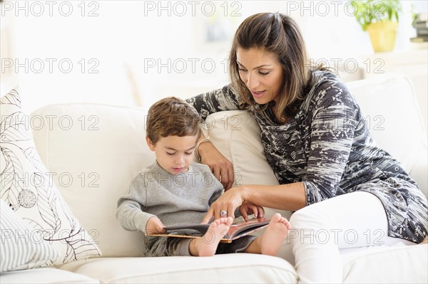 Mother reading with son (2-3) on sofa.