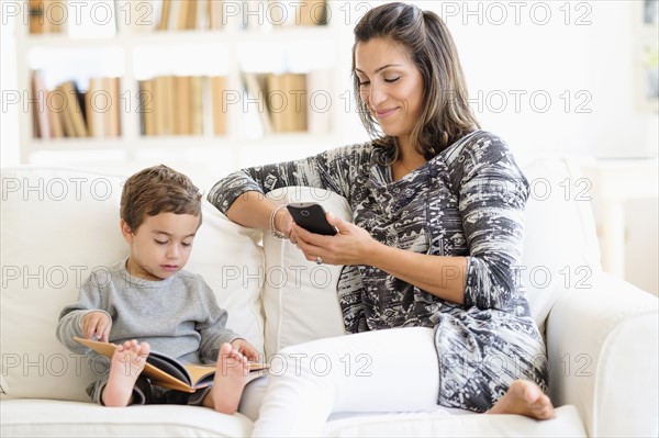 Mother texting while son (2-3) reading on sofa.