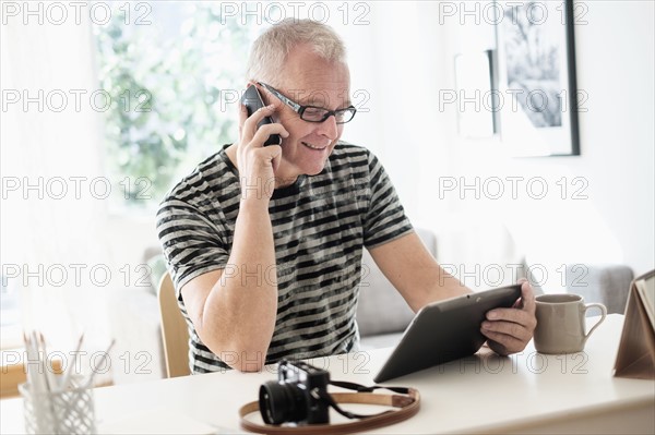 Man in home office using smartphone and tablet.