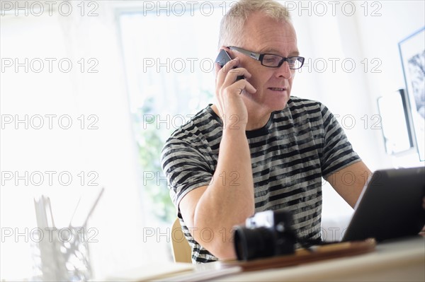 Man in home office using smartphone and tablet.