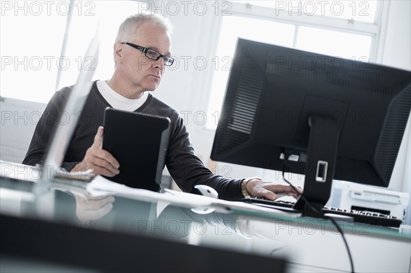 Man working in office using computer and tablet.