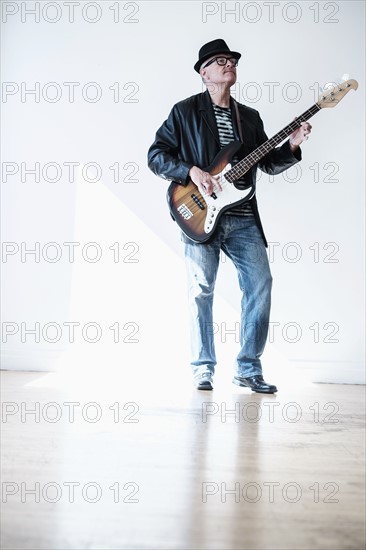 Man playing bass guitar in empty room.