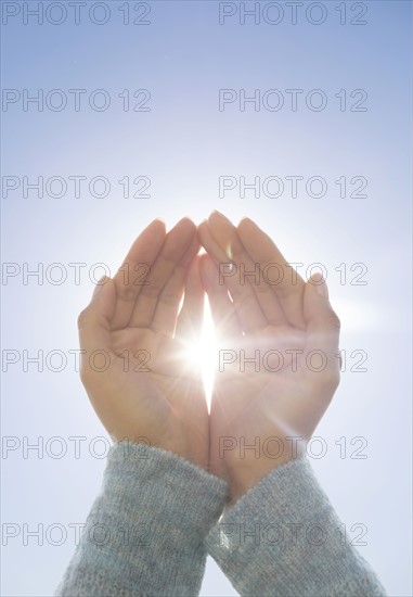 Female hands against clear sky, sun shining through fingers.