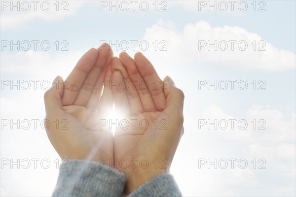 Female hands against clouds, sun shining through fingers.