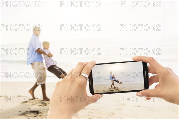 Young woman photographing father with son (12-13) on beach. Jupiter, Florida, USA.