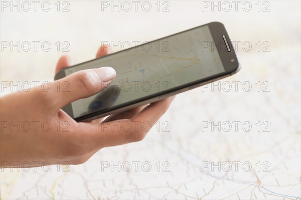 Hand holding smart phone, map in background.