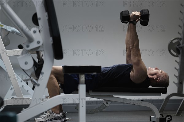 Man exercising with dumbbells on weight bench.