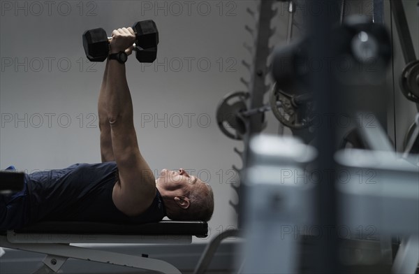 Man exercising with dumbbells on weight bench.