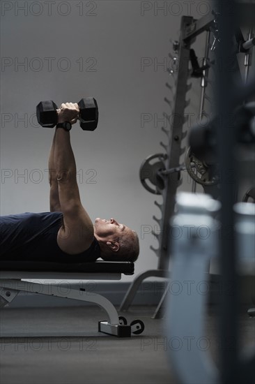 Man exercising with dumbbells on weight bench.