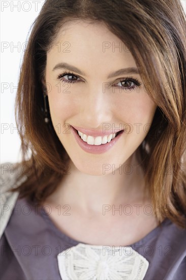 Studio shot portrait of smiling woman with brown hair.