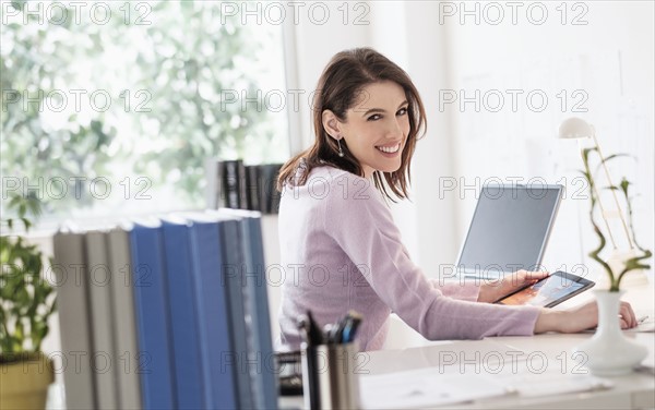 Young woman using digital tablet, looking at camera.