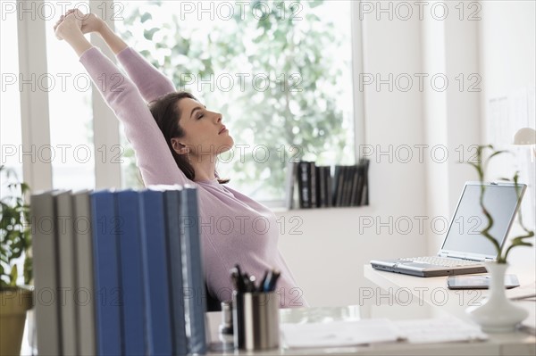 Young woman stretching by desk.