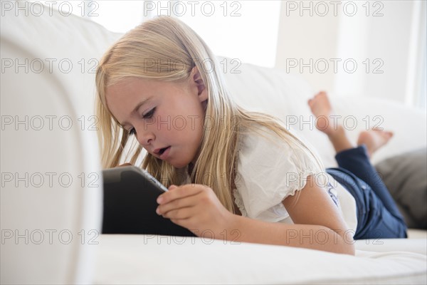 Girl (6-7) using digital tablet on sofa