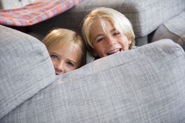 Boy (4-5) and girl (6-7) hiding behind pillows