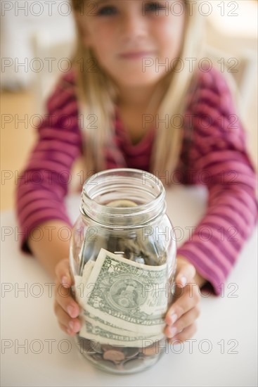 Girl (6-7) holding jar with savings