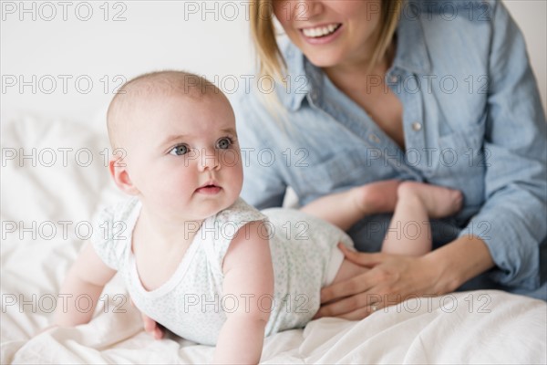 Baby girl (12-17 months) with mother on bed