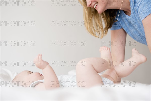 Baby girl (12-17 months) lying down on bed and mother leaning over