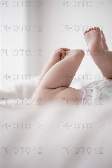 Baby girl (12-17 months) lying down with hands on feet