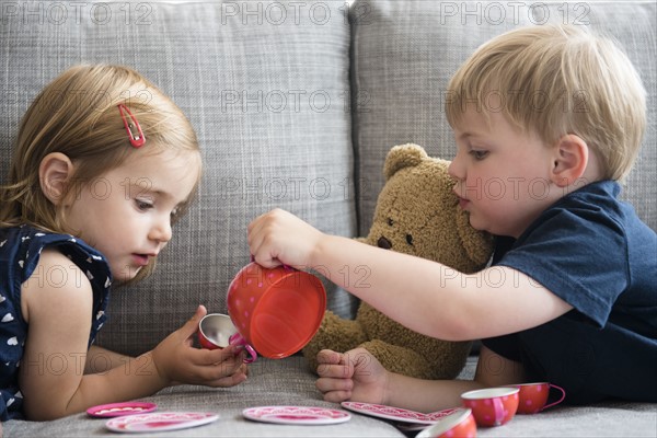 Brother (2-3) and sister (2-3) having tea party with teddy bear