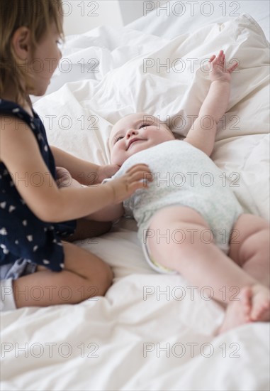 Baby girl (12-17 months) with sister (2-3) on bed