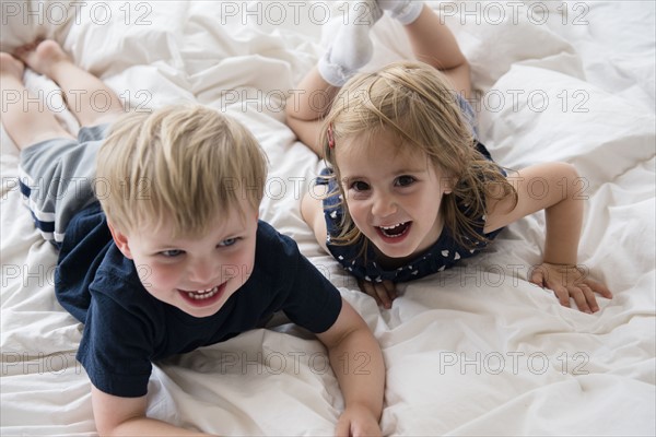 Brother (2-3) with sister (2-3) lying down on bed