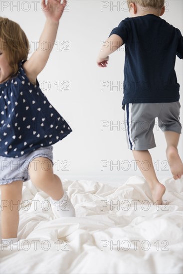 Brother (2-3) with sister (2-3) jumping on bed