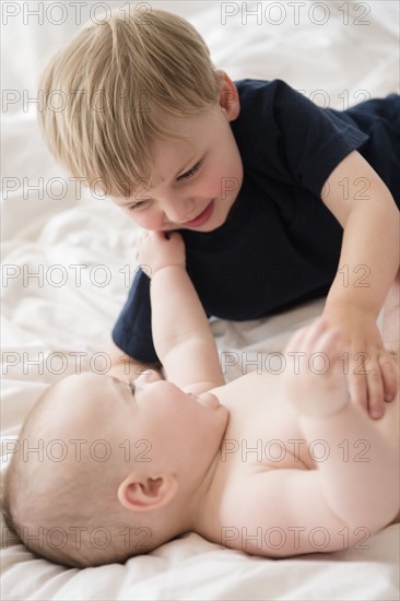 Brother (2-3) playing with baby sister (12-17 months) on bed