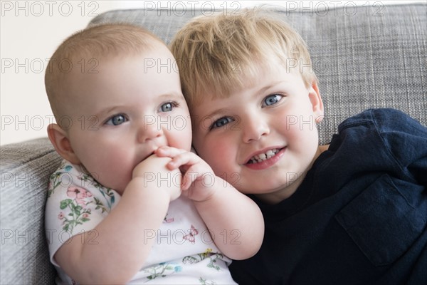 Boy (2-3) with baby sister (12-17 months) sitting on sofa