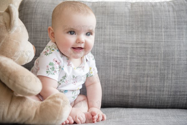 Baby girl (12-17 months) with teddy bear sitting on sofa