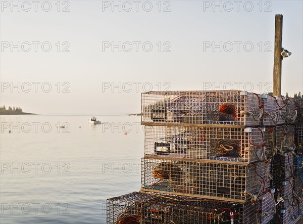 Stacks of lobster traps by sea at sunrise