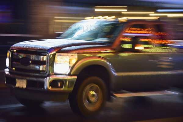 Truck in illuminated city street, in motion at night