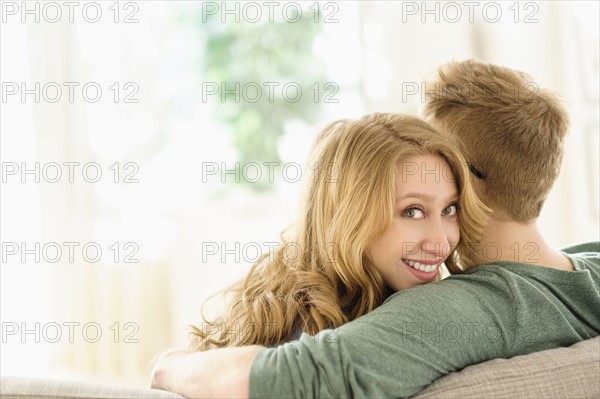 Portrait of young woman hugging boyfriend on sofa.