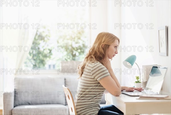 Side-view of young woman working on laptop at home.