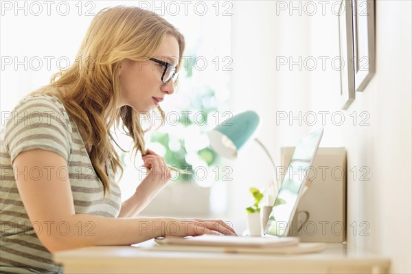 Side-view of young woman working on laptop at home.