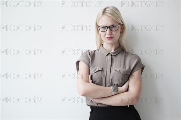 Young woman standing against white wall.