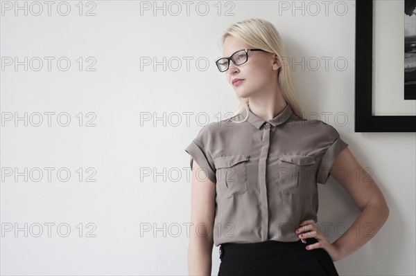 Young woman standing against white wall.