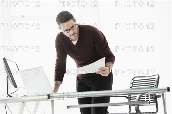 Man using laptop in office, looking at document.