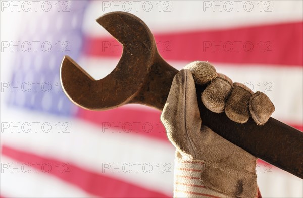 Manual worker's hand holding wrench with American flag in background.