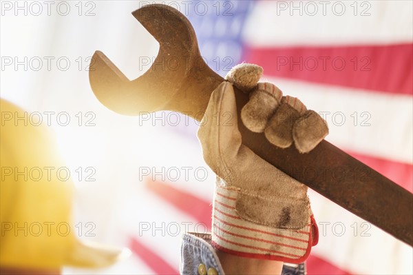 Manual worker's hand holding wrench with American flag in background.