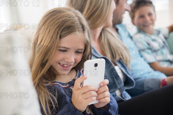 Girl (6-7) sitting on sofa, using smart phone