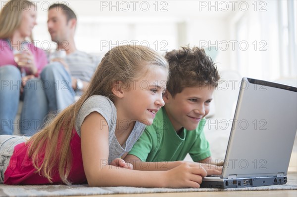 Boy and girl (6-7, 8-9) lying on floor and using laptop
