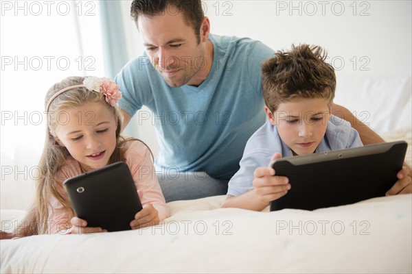 Father with son (8-9) and daughter (6-7) using tablets