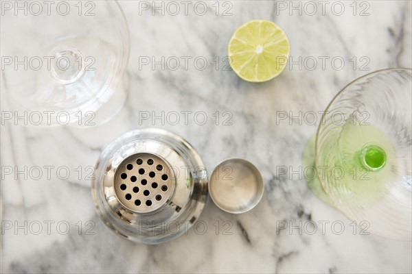 Cocktail in cocktail shaker, martini glasses and halved lime on table