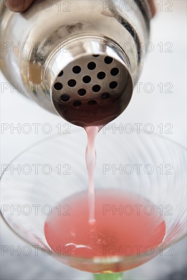 Woman pouring cocktail into martini glass